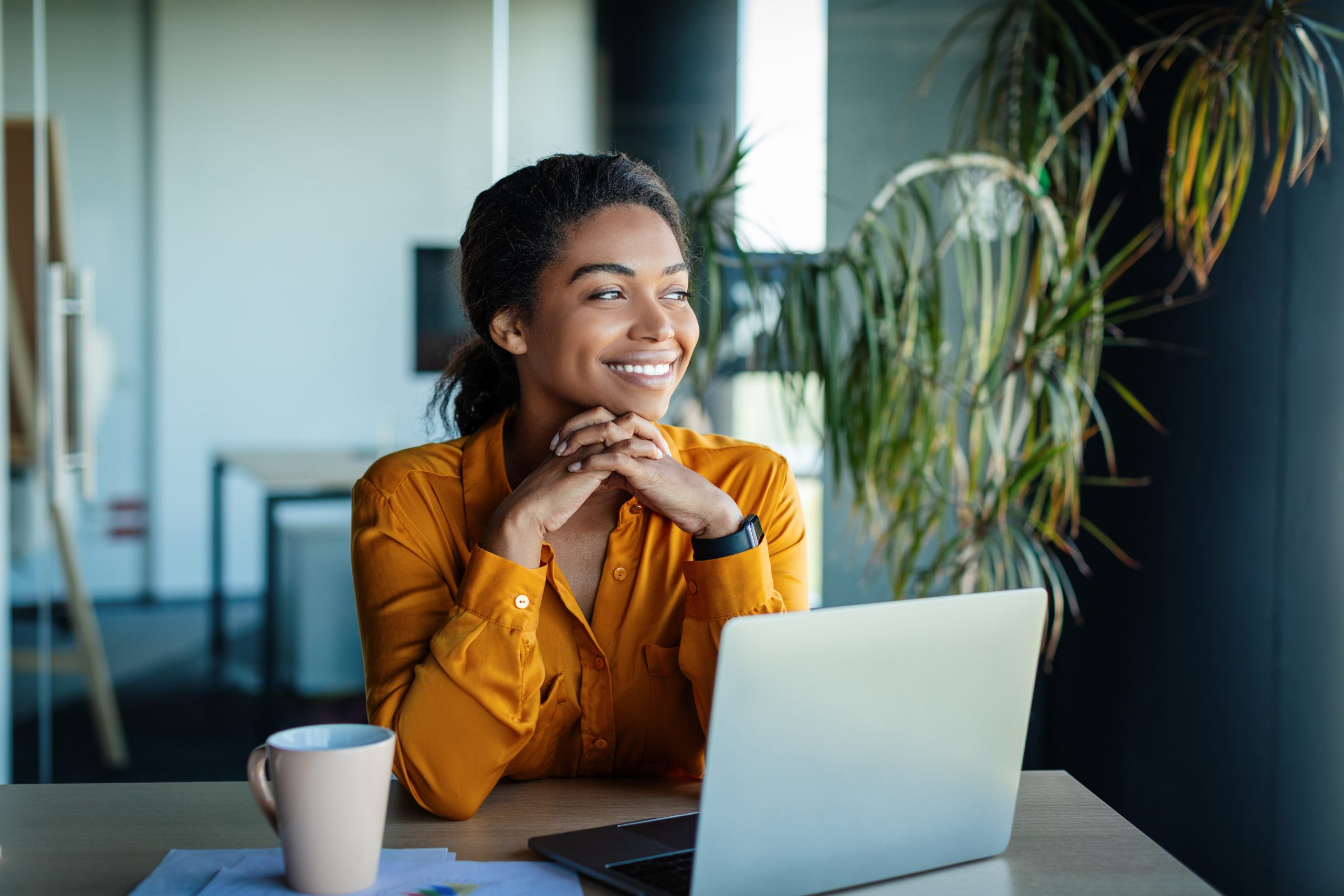 Portrait of dreamy african american businesswoman sitting at desk in office and thinking while working on laptop